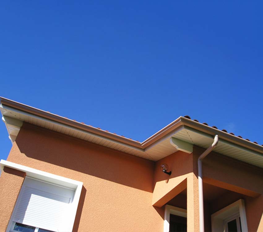 Maison avec gouttières en PVC et ciel bleu