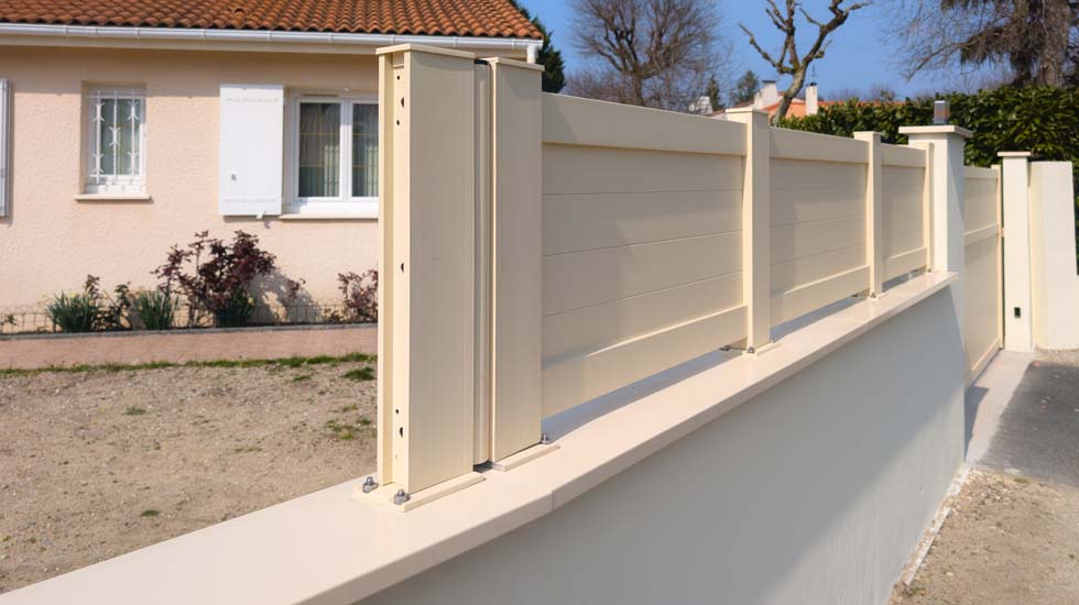 Une barrière métallique avec couvertine est installée et fixée sur le mur de la maison.